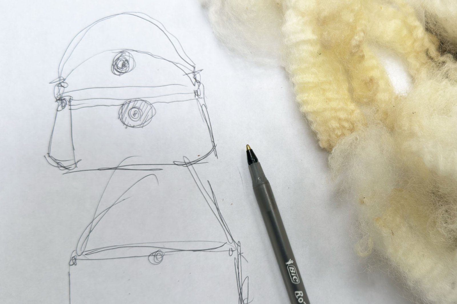 Sketch for the beginning of WOOLBORNE Collection Two beside raw Romney fleece on a studio worktable.