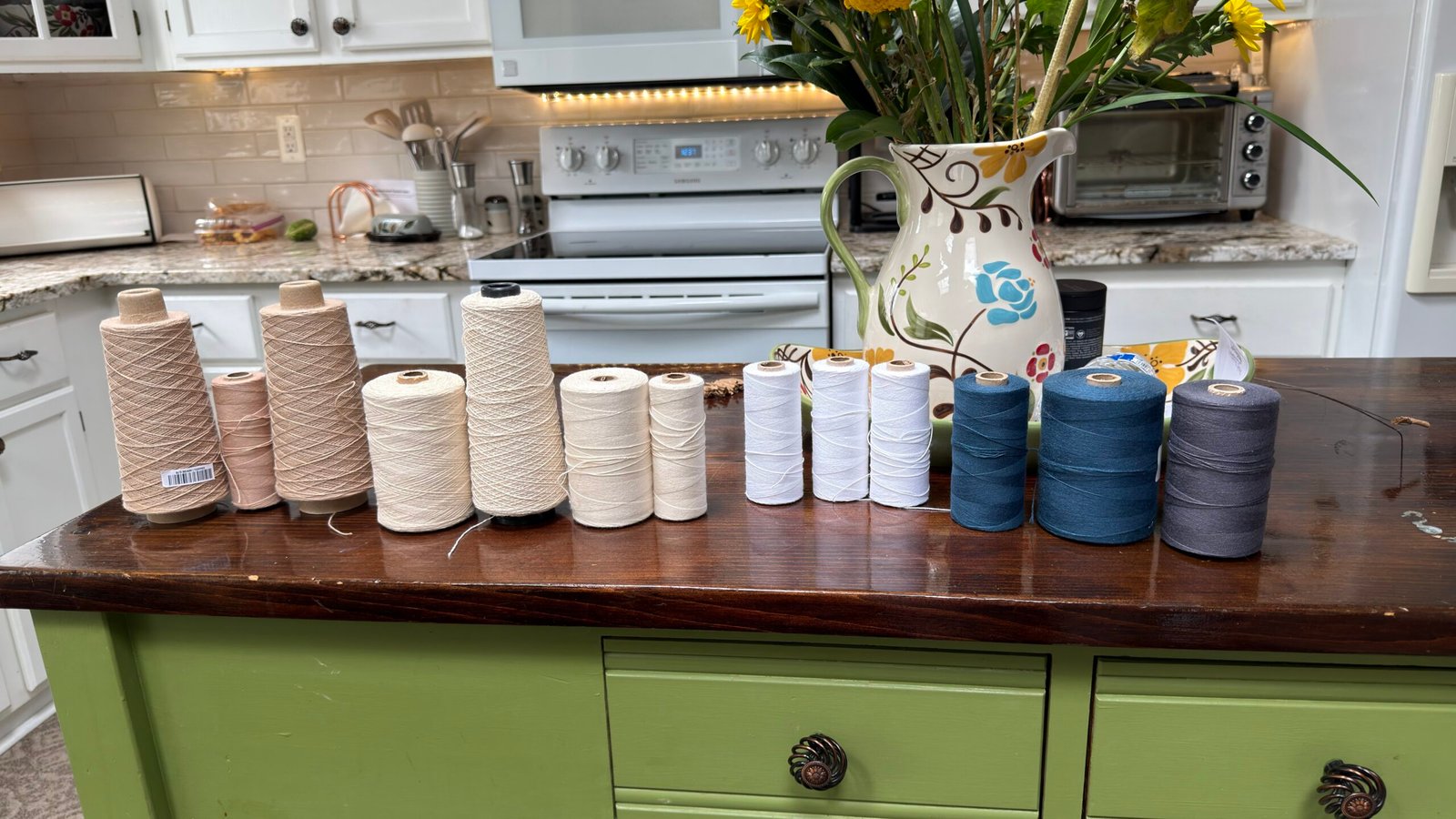 Cones of cotton yarn in natural, cream, white and blue tones arranged across a kitchen island while selecting colors for a handwoven towel warp.